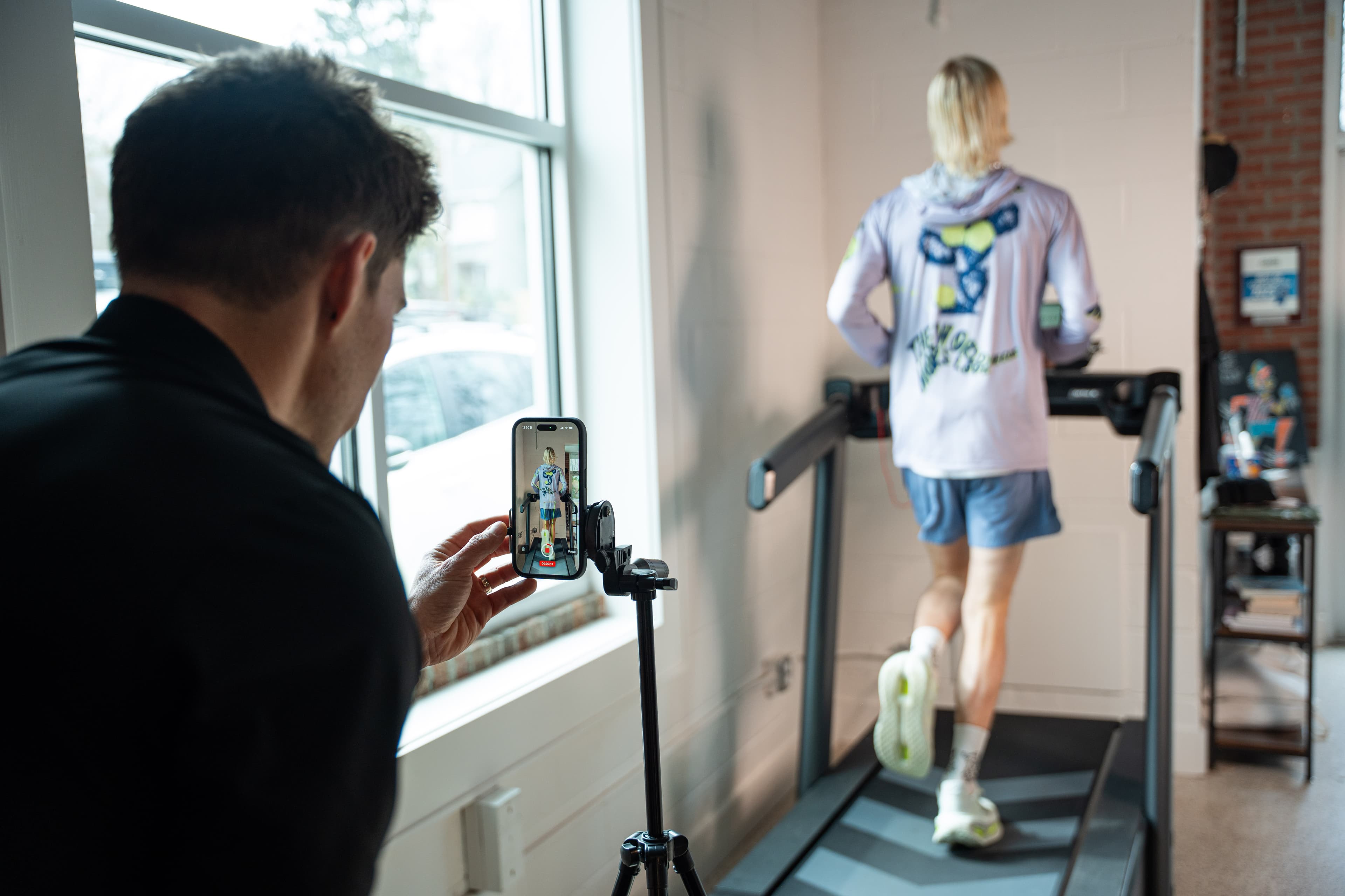Physical therapist recording a runner on a treadmill with a smartphone during a gait analysis at Swamp Rabbit Physiotherapy