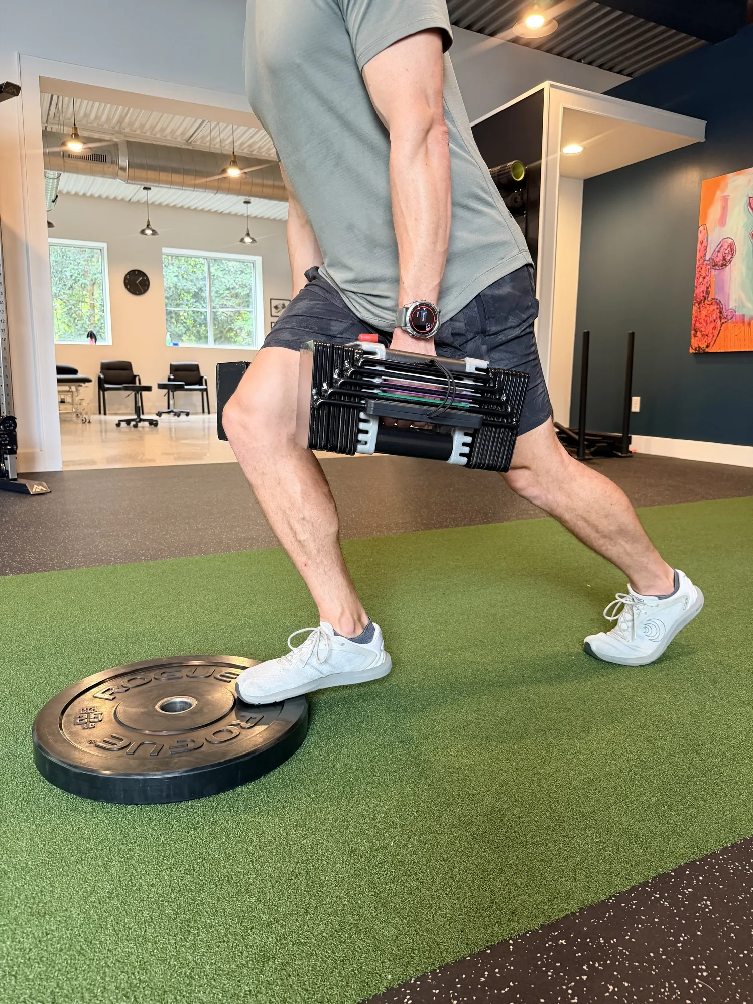 Runner performing a single-leg calf raise with the forefoot on a weight plate while holding a dumbbell, showing that simple equipment can load the calf-Achilles system, at Swamp Rabbit Physiotherapy in Greenville, SC